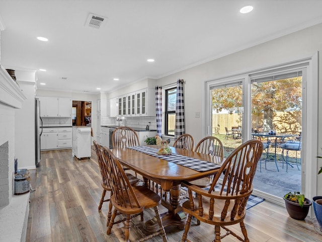 dining space featuring crown molding, a brick fireplace, and light wood-type flooring