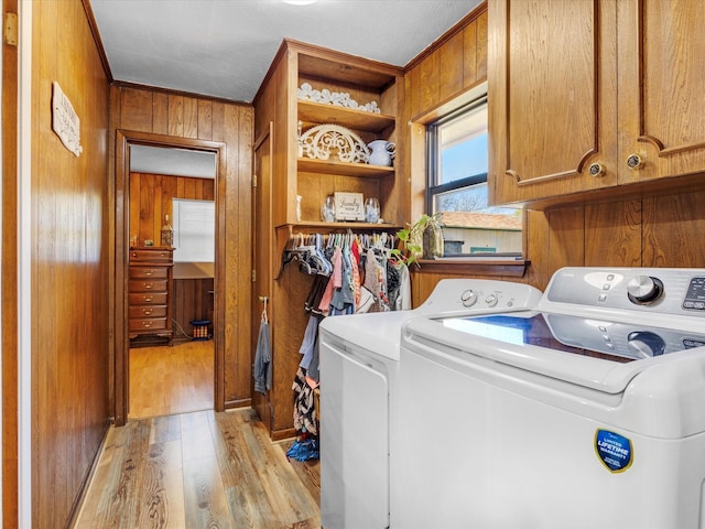 washroom with wooden walls, light hardwood / wood-style floors, cabinets, and washing machine and clothes dryer