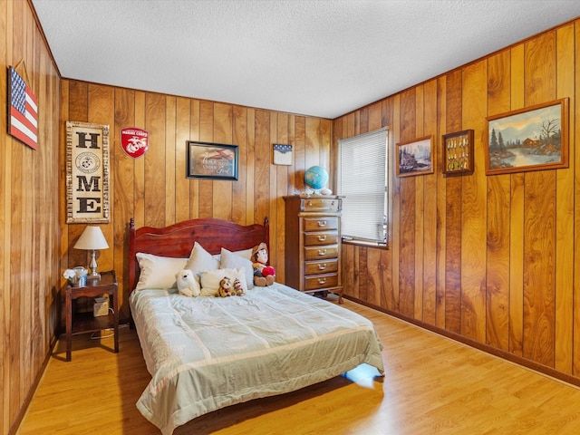 bedroom with light hardwood / wood-style flooring, a textured ceiling, and wood walls