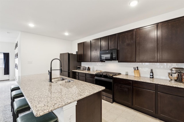 kitchen with black appliances, a kitchen breakfast bar, sink, light stone countertops, and an island with sink