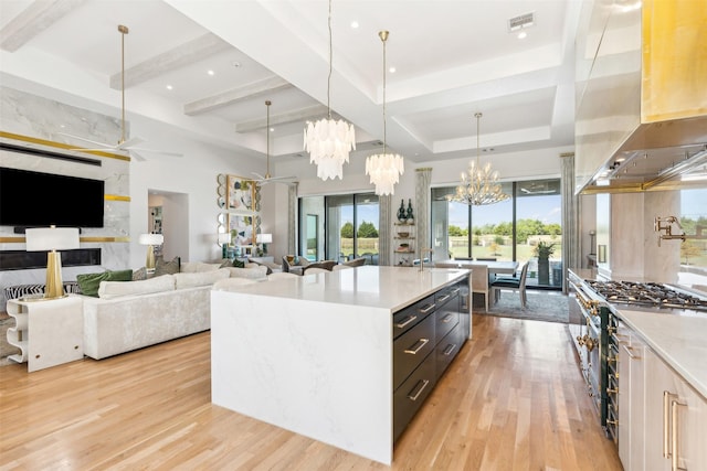 kitchen with island range hood, light wood-type flooring, an island with sink, a notable chandelier, and pendant lighting