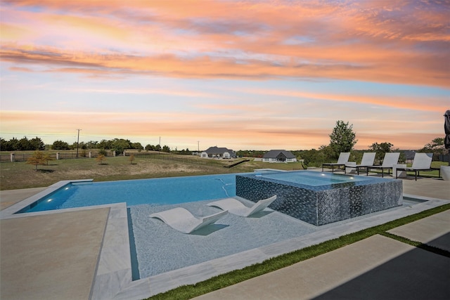 pool at dusk featuring a patio and an in ground hot tub