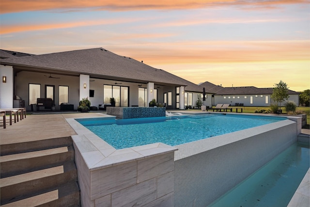 pool at dusk featuring ceiling fan and a patio area