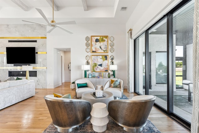 living room with beamed ceiling, ceiling fan, a wealth of natural light, and light wood-type flooring