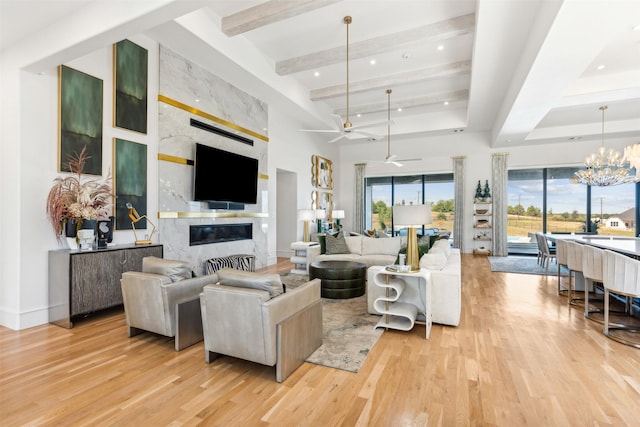 living room with beam ceiling, light hardwood / wood-style floors, a premium fireplace, ceiling fan with notable chandelier, and a high ceiling