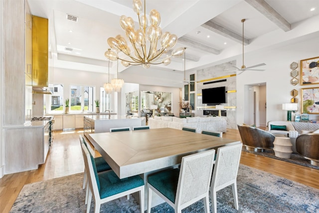 dining area featuring a towering ceiling, ceiling fan with notable chandelier, sink, beam ceiling, and light hardwood / wood-style flooring