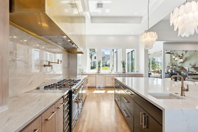 kitchen featuring hanging light fixtures, sink, light stone counters, and light hardwood / wood-style flooring