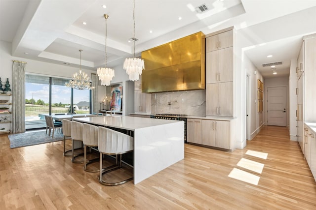 kitchen featuring wall chimney range hood, pendant lighting, a center island with sink, and a tray ceiling