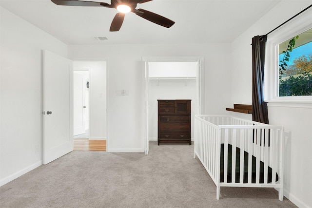 unfurnished bedroom with ceiling fan, a closet, light colored carpet, and a crib