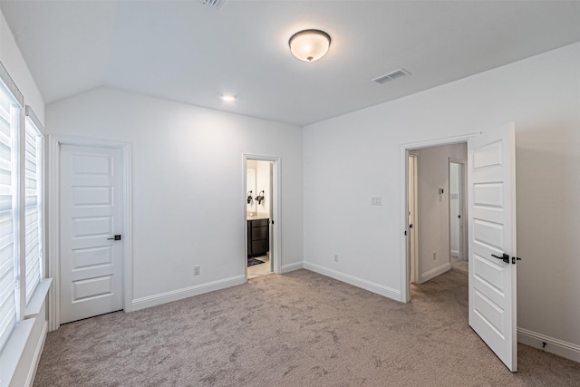 unfurnished bedroom featuring light colored carpet, ensuite bathroom, and vaulted ceiling