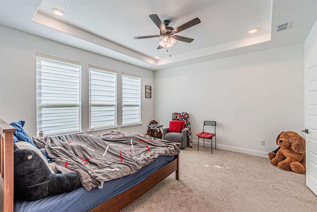 carpeted bedroom with ceiling fan, multiple windows, and a tray ceiling