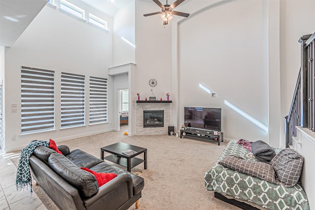 living room with ceiling fan, a stone fireplace, a high ceiling, and light colored carpet