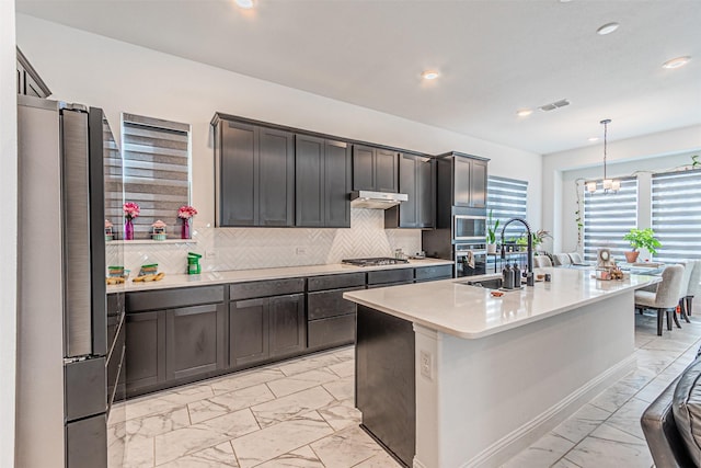 kitchen featuring hanging light fixtures, appliances with stainless steel finishes, sink, tasteful backsplash, and a center island with sink