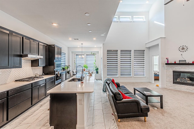 kitchen with stainless steel gas stovetop, hanging light fixtures, sink, a kitchen island with sink, and decorative backsplash