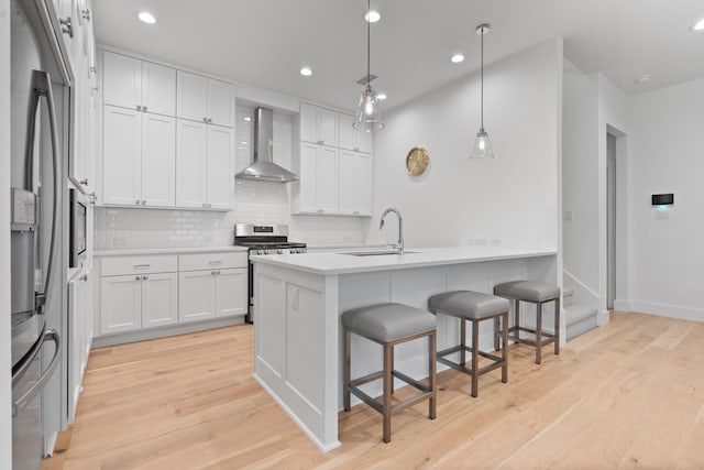 kitchen featuring white cabinetry, wall chimney range hood, sink, and appliances with stainless steel finishes