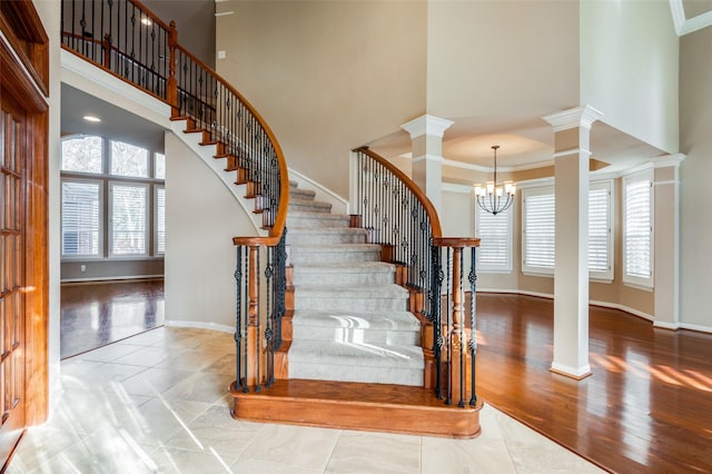 staircase with a notable chandelier, ornamental molding, a towering ceiling, and decorative columns