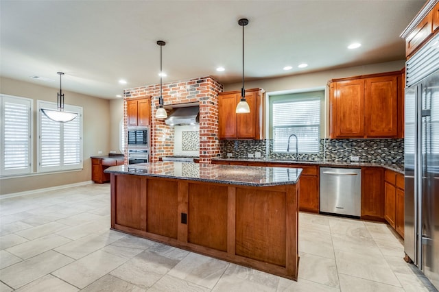 kitchen featuring appliances with stainless steel finishes, dark stone counters, pendant lighting, wall chimney exhaust hood, and a center island