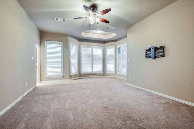 empty room featuring ceiling fan, light carpet, and a raised ceiling