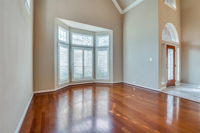 foyer with high vaulted ceiling, a wealth of natural light, crown molding, and hardwood / wood-style floors