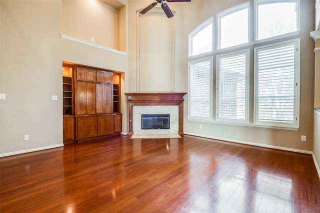 unfurnished living room featuring a high ceiling, ceiling fan, hardwood / wood-style flooring, and a tile fireplace