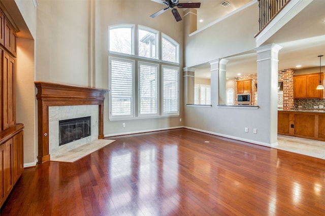 unfurnished living room with ceiling fan, a tile fireplace, wood-type flooring, a towering ceiling, and ornate columns