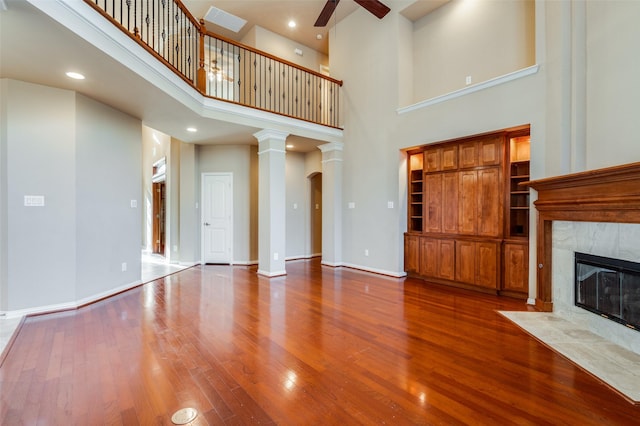 unfurnished living room with decorative columns, ceiling fan, a high ceiling, a fireplace, and wood-type flooring