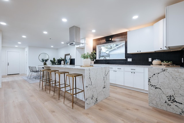 kitchen with light stone counters, island exhaust hood, a kitchen island, light wood-type flooring, and white cabinets