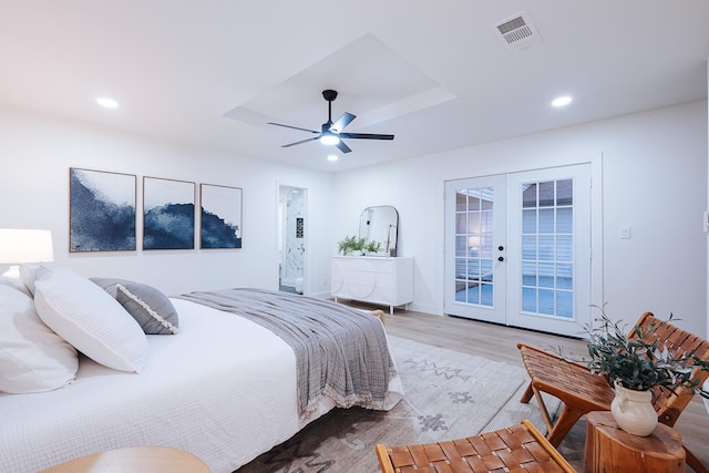 bedroom featuring hardwood / wood-style flooring, ceiling fan, french doors, a tray ceiling, and access to exterior