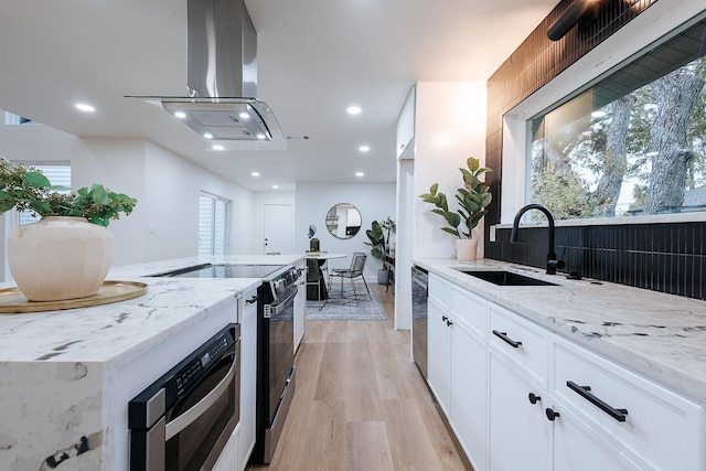 kitchen with sink, stainless steel appliances, white cabinetry, light stone countertops, and island range hood