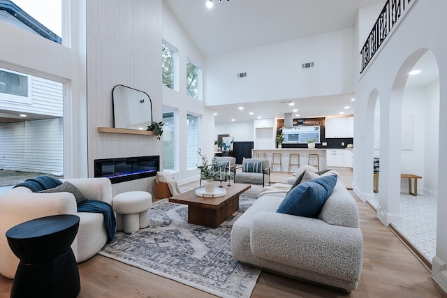 living room featuring a towering ceiling, light wood-type flooring, and a large fireplace