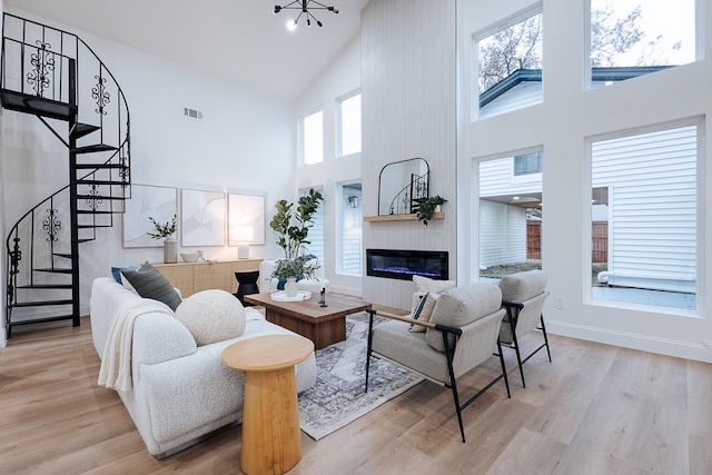 living room featuring a notable chandelier, light hardwood / wood-style flooring, a towering ceiling, and a fireplace