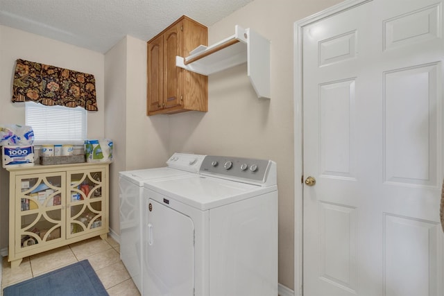 clothes washing area featuring washer and clothes dryer, light tile patterned floors, cabinets, and a textured ceiling