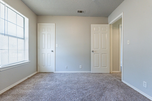 unfurnished bedroom featuring carpet, a textured ceiling, and multiple windows