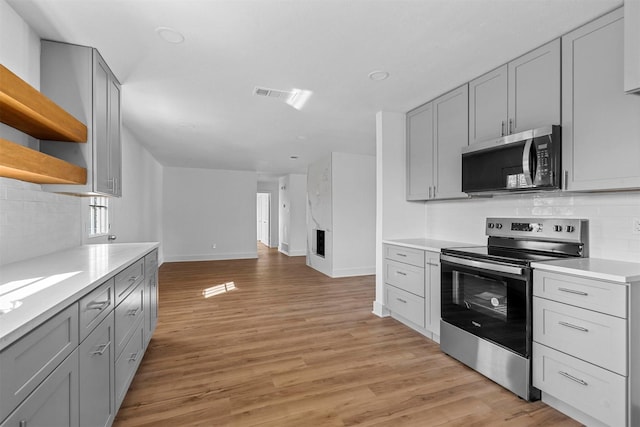 kitchen with gray cabinets, backsplash, appliances with stainless steel finishes, and light hardwood / wood-style flooring