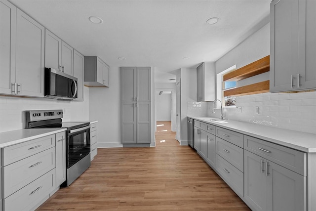 kitchen with appliances with stainless steel finishes, sink, gray cabinetry, backsplash, and light hardwood / wood-style flooring