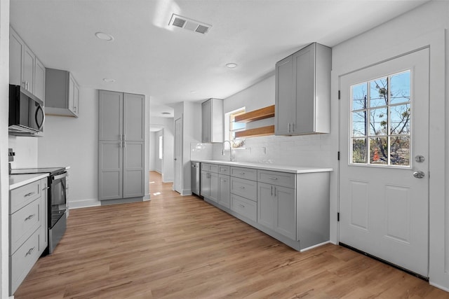 kitchen featuring gray cabinetry, sink, appliances with stainless steel finishes, tasteful backsplash, and light hardwood / wood-style floors