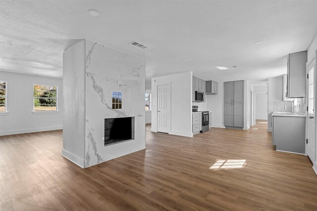 unfurnished living room with a textured ceiling, sink, light wood-type flooring, and a fireplace