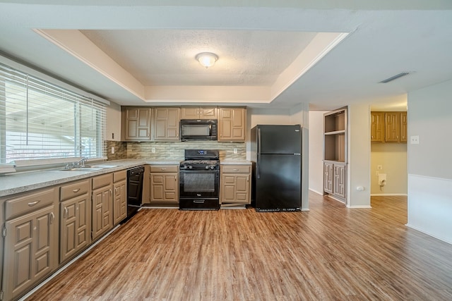 kitchen with a tray ceiling, sink, black appliances, and light hardwood / wood-style floors