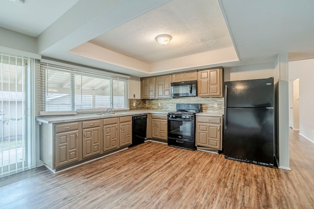 kitchen with a tray ceiling, light hardwood / wood-style flooring, a healthy amount of sunlight, and black appliances