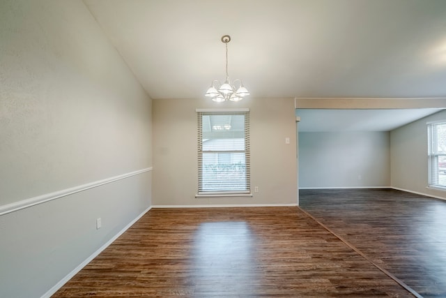 empty room with dark wood-type flooring, lofted ceiling, and a notable chandelier