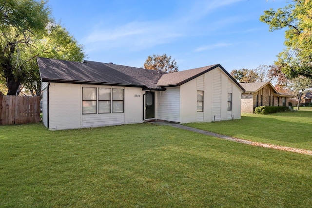 view of front of property featuring a shingled roof, a front yard, brick siding, and fence