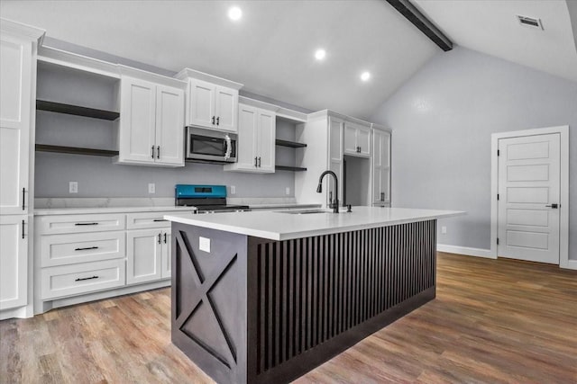 kitchen with beam ceiling, black stove, sink, a center island with sink, and white cabinets