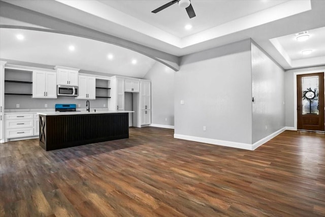 kitchen with stove, a kitchen island with sink, white cabinets, sink, and dark hardwood / wood-style floors