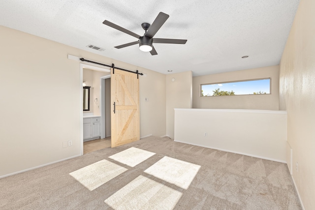 empty room with ceiling fan, a textured ceiling, a barn door, light carpet, and visible vents