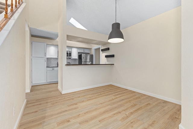 unfurnished living room with stairs, lofted ceiling, light wood-style flooring, and baseboards