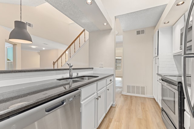 kitchen with sink, stainless steel appliances, dark stone countertops, pendant lighting, and white cabinets