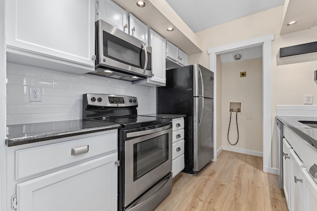 kitchen with tasteful backsplash, white cabinets, dark stone countertops, stainless steel appliances, and light wood-type flooring