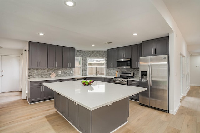 kitchen with sink, stainless steel appliances, light hardwood / wood-style floors, decorative backsplash, and a kitchen island