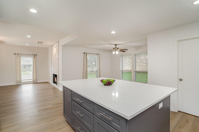 kitchen with a fireplace, light hardwood / wood-style floors, a center island, and ceiling fan