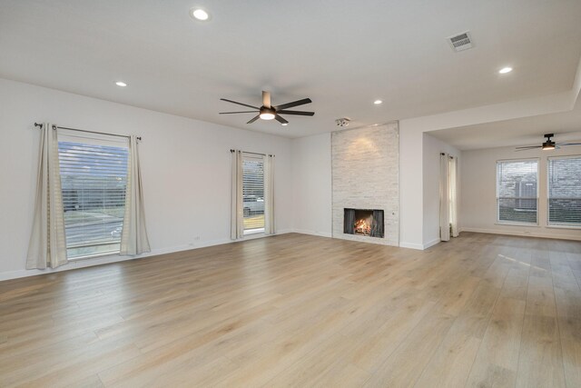 unfurnished living room with ceiling fan, a stone fireplace, and light wood-type flooring